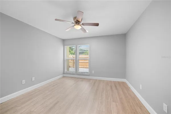 an empty room with wooden floor fan and windows