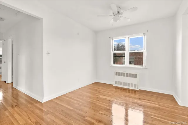 a view of an empty room with wooden floor and a ceiling fan