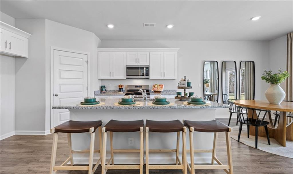 205 Storm Lane Hoschton, GA 30548 - Photo 10 of 51 a kitchen with stainless steel appliances kitchen island granite countertop a dining table chairs and a refrigerator