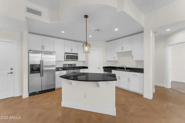 a kitchen with stainless steel appliances granite countertop a sink a stove a refrigerator and white cabinets