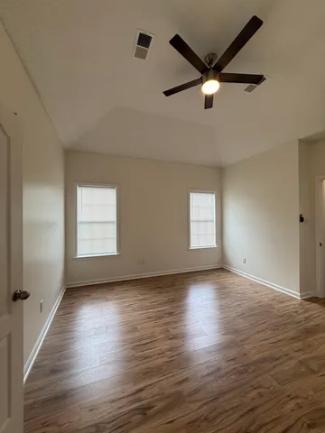 an empty room with wooden floor a ceiling fan and windows