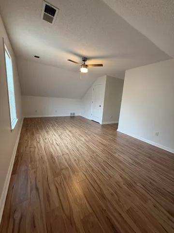 an empty room with wooden floor fan and windows