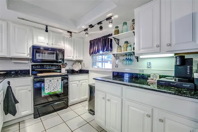 a kitchen with granite countertop a sink a stove a microwave a refrigerator and cabinets