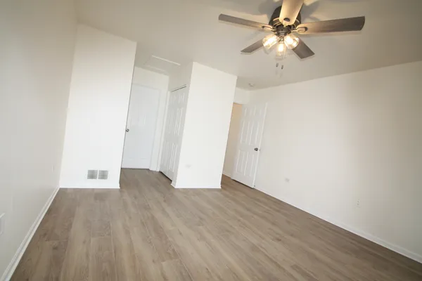 an empty room with wooden floor fan and windows