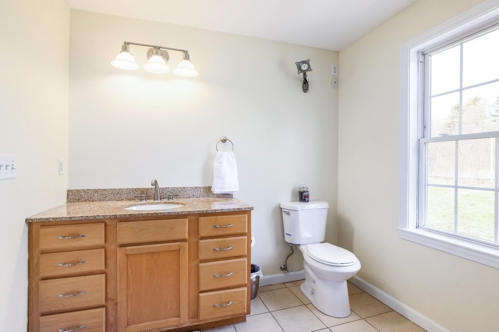 53 Baker Pond Road Charlton, MA 01507 - Photo 26 of 27 a bathroom with a granite countertop toilet a sink and a window
