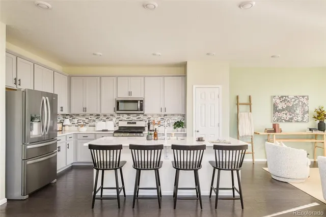 a kitchen with stainless steel appliances kitchen island granite countertop a dining table chairs and a refrigerator