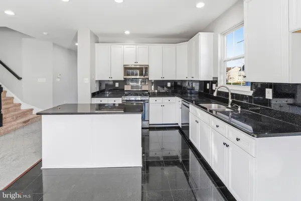 a kitchen with stainless steel appliances granite countertop a refrigerator a stove a sink dishwasher and white cabinets with wooden floor