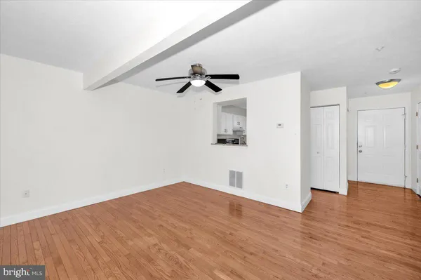 a view of an empty room with wooden floor and a ceiling fan
