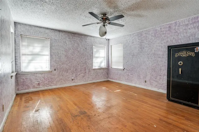 an empty room with wooden floor fan and windows