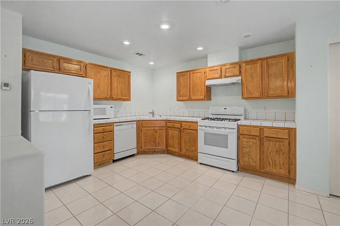 2243 Rugged Mesa Drive Laughlin, NV 89029 - Photo 9 of 32 A functional kitchen features wood cabinetry, white appliances, and tiled flooring.