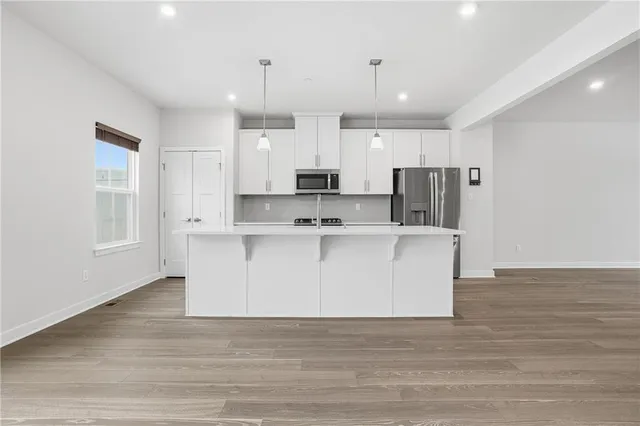 a view living room with stainless steel appliances kitchen island granite countertop a refrigerator a stove a sink and white cabinets with wooden floor