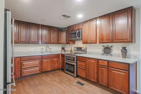 a kitchen with stainless steel appliances granite countertop wooden cabinets a sink and dishwasher a stove top oven with wooden floor