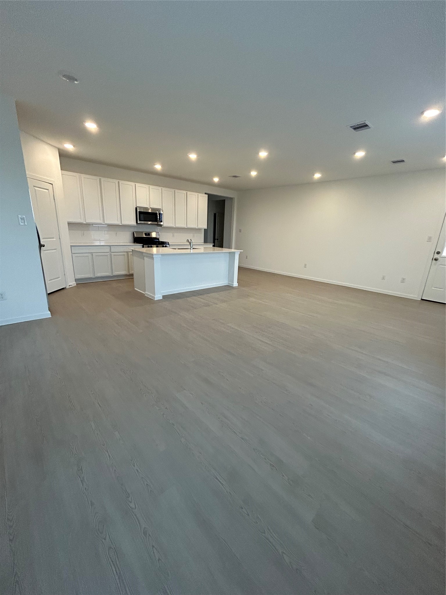 26419 Virginia Wild Rye Lane Katy, TX 77493 - Photo 9 of 31 Spacious open-concept area with modern kitchen featuring white cabinets, an island with a sink, stainless steel appliances, and recessed lighting. The room has sleek flooring and ample space for living and dining.