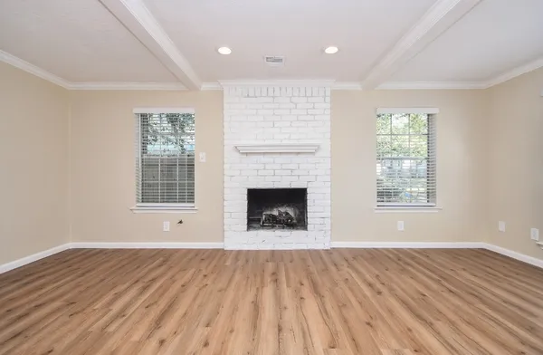 a view of an empty room with wooden floor a fireplace and a window