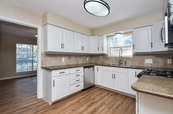 a kitchen with granite countertop wooden cabinets a stove a sink and dishwasher with wooden floor