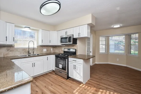 a kitchen with granite countertop a stove top oven a sink dishwasher and white cabinets with wooden floor