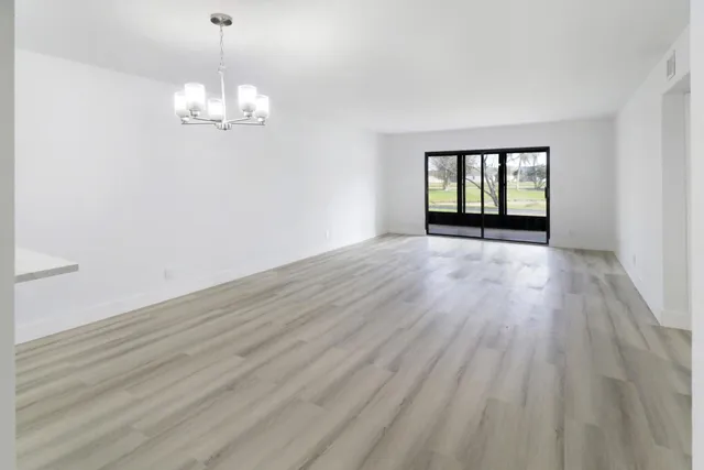 an empty room with wooden floor chandelier and windows