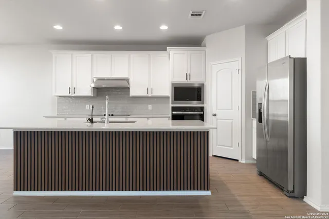 a kitchen with stainless steel appliances granite countertop a refrigerator a sink dishwasher a oven and a microwave with wooden floor