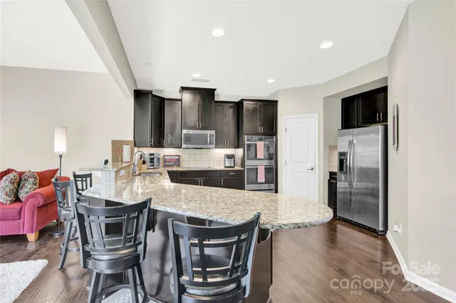a kitchen with stainless steel appliances kitchen island granite countertop a table chairs refrigerator and microwave
