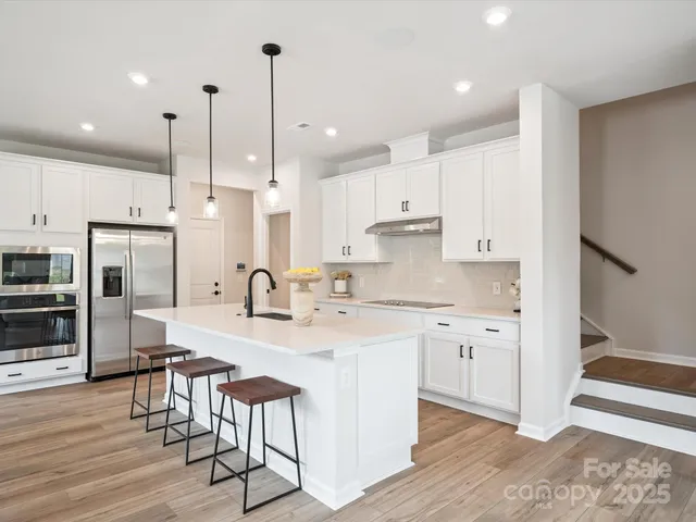 a kitchen with stainless steel appliances granite countertop a stove a sink a refrigerator and white cabinets with wooden floor