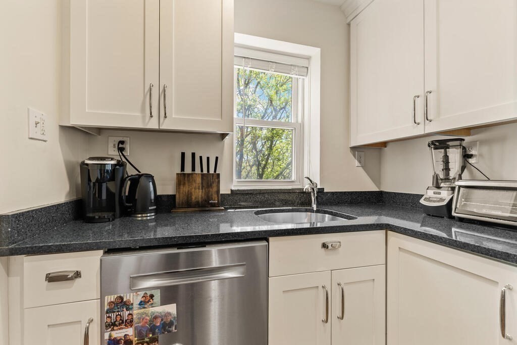 395 Broadway, Unit R5E Cambridge, MA 02139 - Photo 14 of 27 a kitchen with granite countertop a sink stainless steel appliances white cabinets and a window