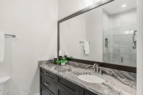 a bathroom with a granite countertop sink a toilet a mirror and shower