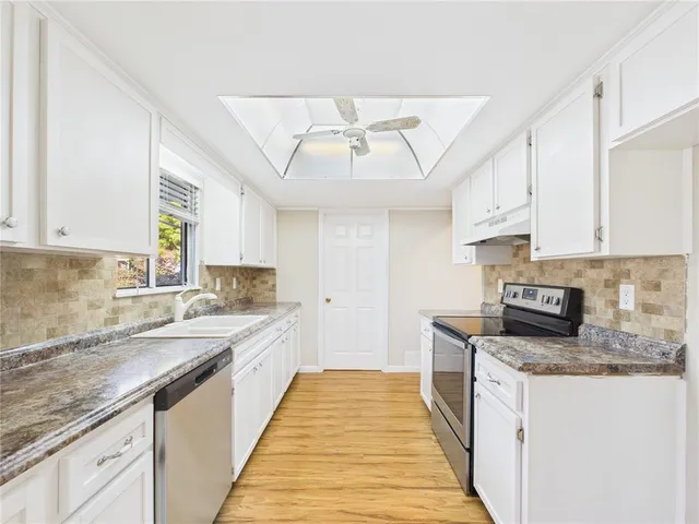 a large kitchen with stainless steel appliances granite countertop a sink and dishwasher a stove top oven with white cabinets