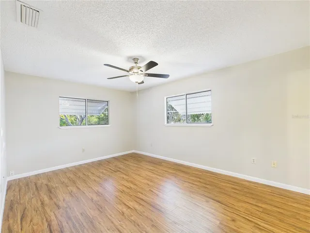 a view of an empty room with wooden floor and a ceiling fan