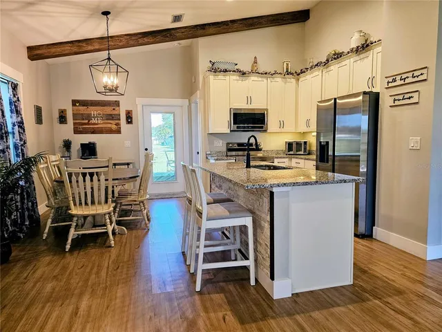 a kitchen with stainless steel appliances a stove top oven a refrigerator a dining table and chairs with wooden floor