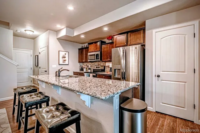 a kitchen with stainless steel appliances granite countertop a refrigerator a stove and a sink with wooden floor