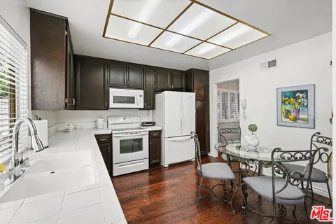 a kitchen with stainless steel appliances a stove a sink dishwasher a refrigerator with a dining table and chairs