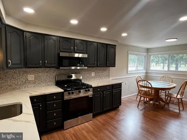 a kitchen with granite countertop wooden floors appliances and wooden cabinets