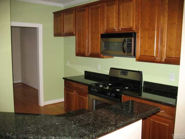 6102 Shandwick Court Raleigh, NC 27609 - Photo 4 of 10 Kitchen with stain cabinets, granite countertops, gas range and spacesaver microwave.