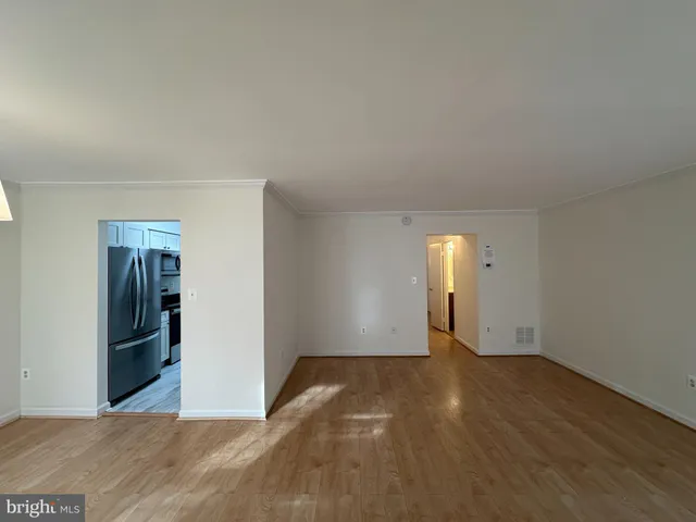 a view of an empty room with wooden floor and a kitchen