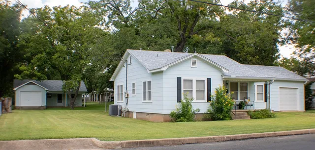 a view of a house with a yard plants and large tree