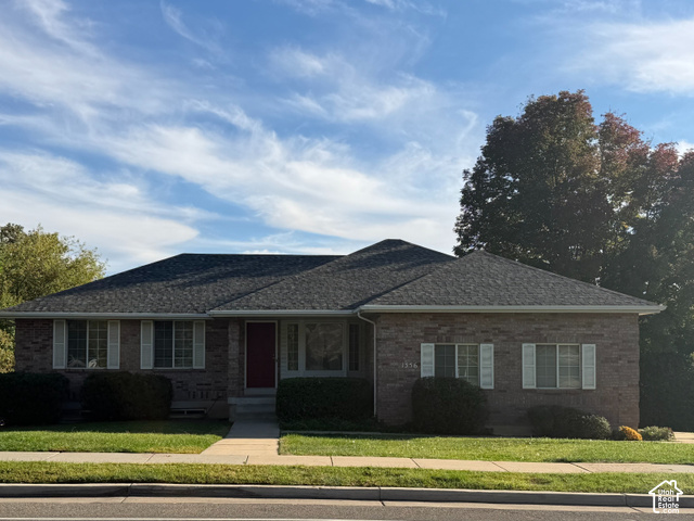 1356 Nicholls Road Fruit Heights, UT 84037 - Photo 1 of 1 Brick-clad exterior with a dark roof, front yard with manicured lawn, concrete walkway, and mature trees