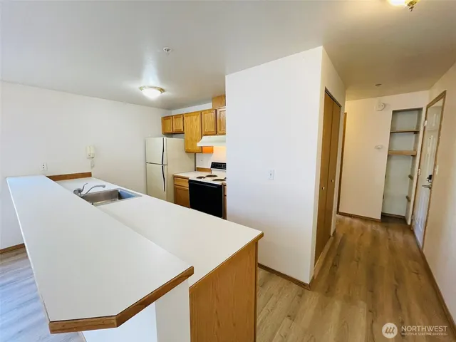 a kitchen with granite countertop a refrigerator a stove a sink dishwasher and wooden cabinets with wooden floor