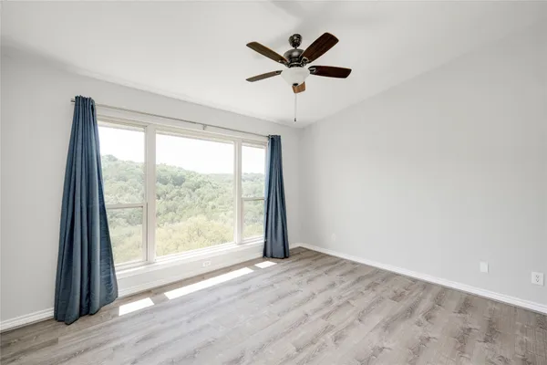 an empty room with wooden floor fan and windows