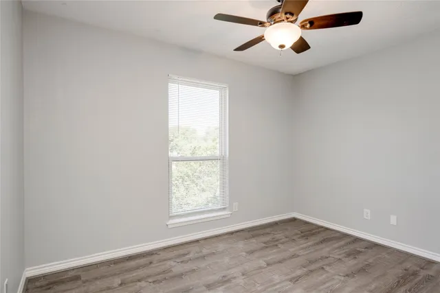 an empty room with wooden floor fan and windows