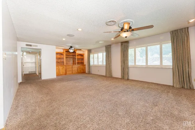an empty room with chandelier fan and windows
