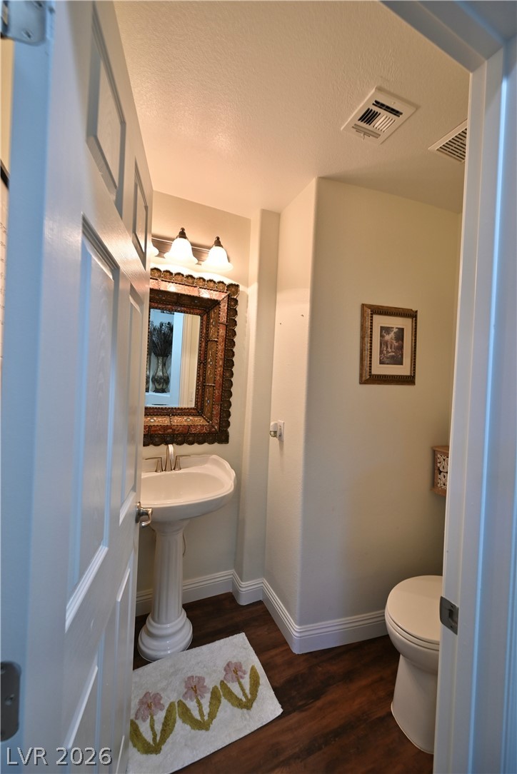 2729 Kildrummie Street Henderson, NV 89044 - Photo 18 of 42 A compact half bath with a classic pedestal sink, rich wood flooring, and a warmly lit mirror.