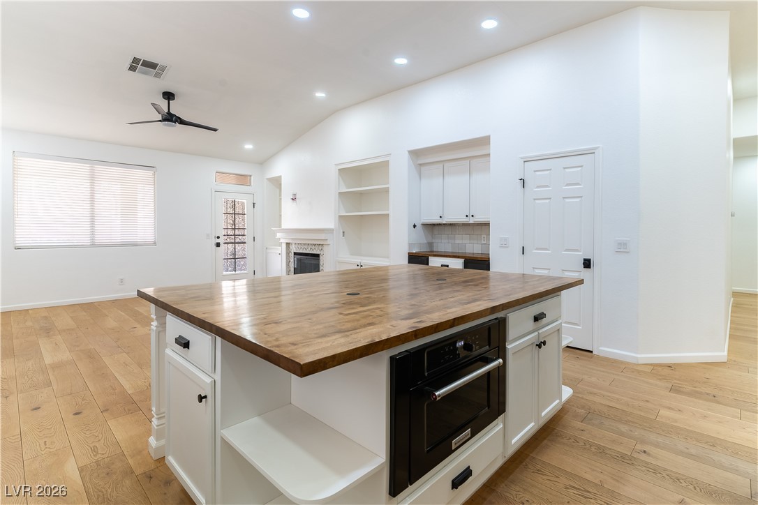 Kitchen with Butcher Block countertop, white cabinetry, a fireplace, French Oak flooring, and recessed lighting