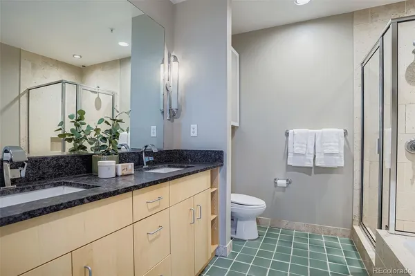 a bathroom with a granite countertop sink a toilet a large mirror and shower