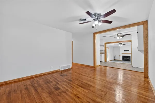 a view of an empty room with wooden floor and a ceiling fan