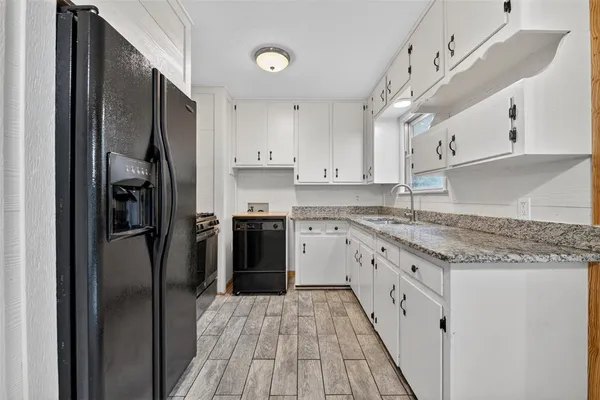 a kitchen with granite countertop a refrigerator oven a sink dishwasher and white cabinets with wooden floor