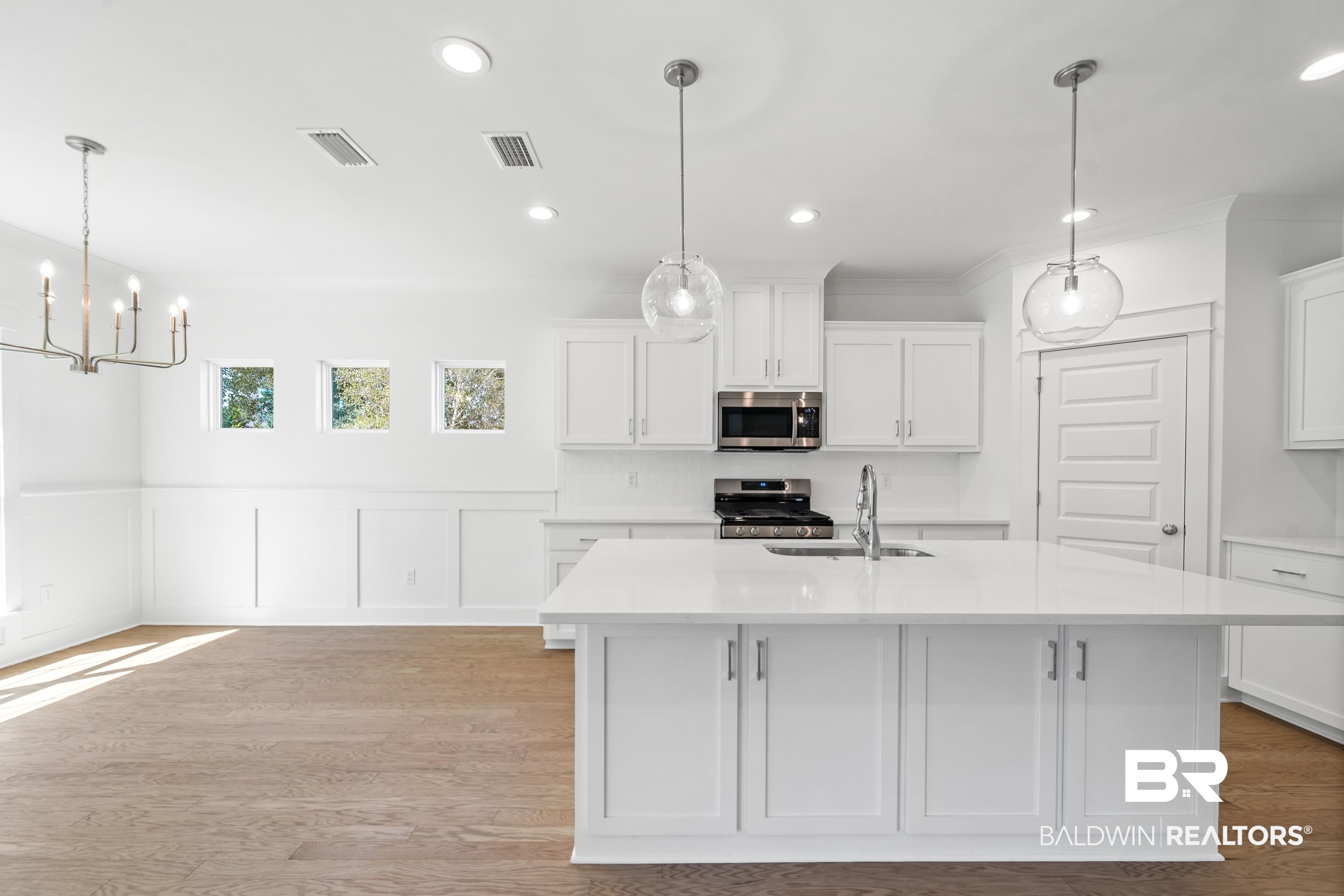 25927 Capra Court Daphne, AL 36526 - Photo 14 of 37 Kitchen with white cabinets, an island with sink, decorative light fixtures, stainless steel appliances, and light hardwood / wood-style floors
