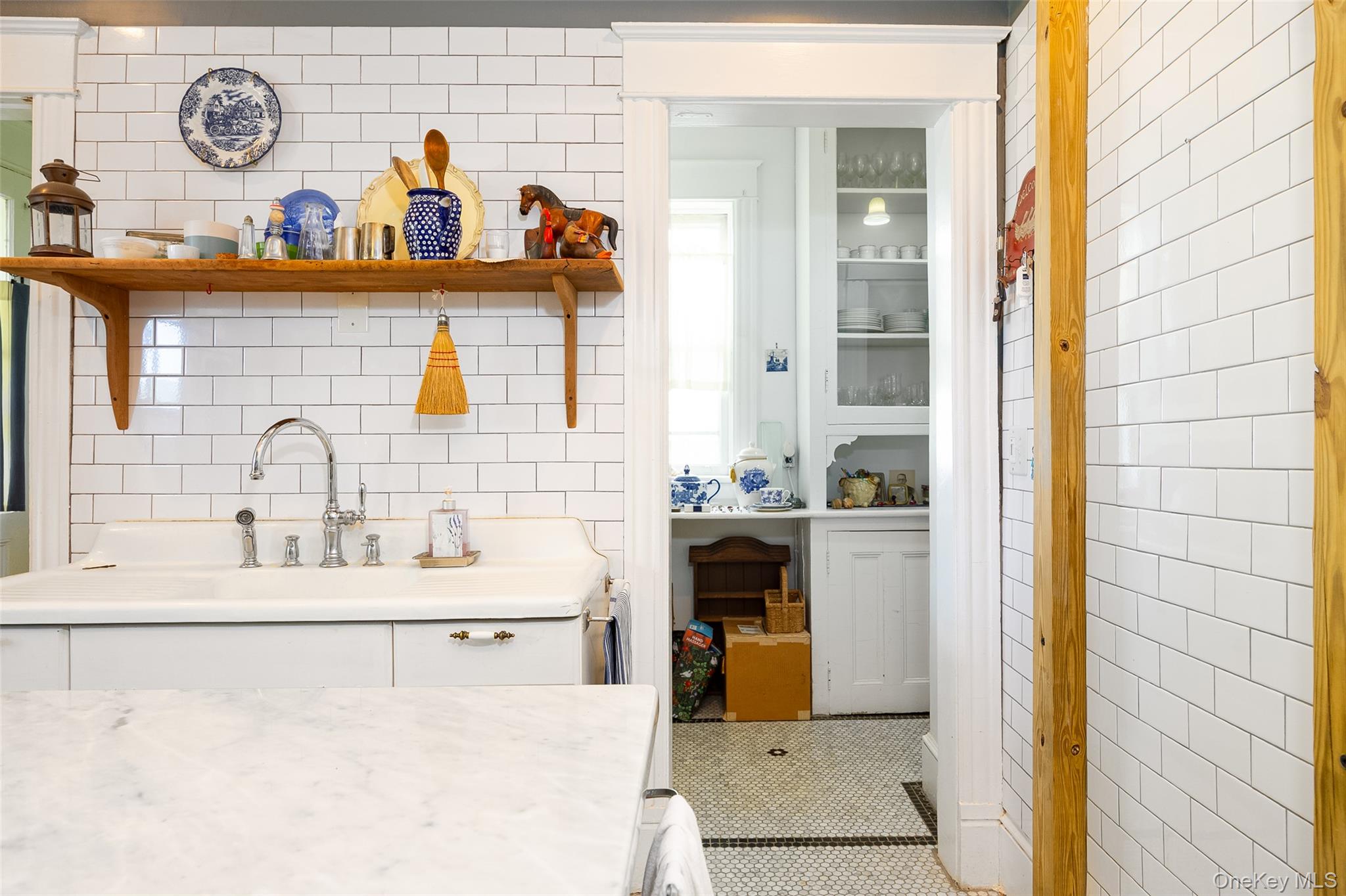 111 South Hamilton Street Poughkeepsie, NY 12601 - Photo 13 of 33 Kitchen area featuring white subway tile backsplash, a large white basin sink with a chrome faucet, a floating wood shelf, and a built-in pantry with glass-front cabinetry