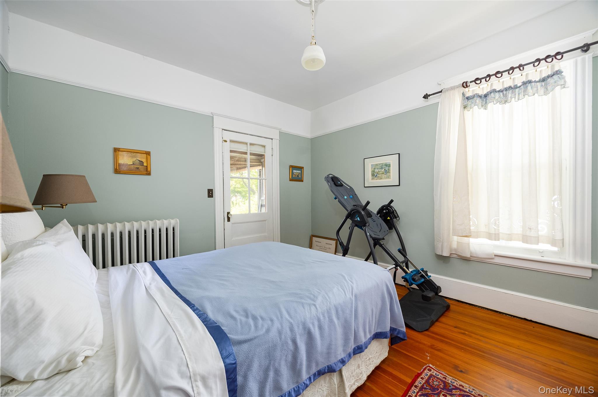111 South Hamilton Street Poughkeepsie, NY 12601 - Photo 15 of 33 Hardwood flooring complements the light green wall color in this room, featuring a white window with a sheer curtain, a white radiator, and a white paneled door