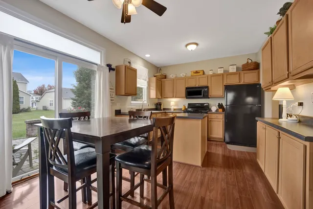 a kitchen with stainless steel appliances granite countertop a stove top oven a sink a refrigerator with a dining table and chairs with wooden floor