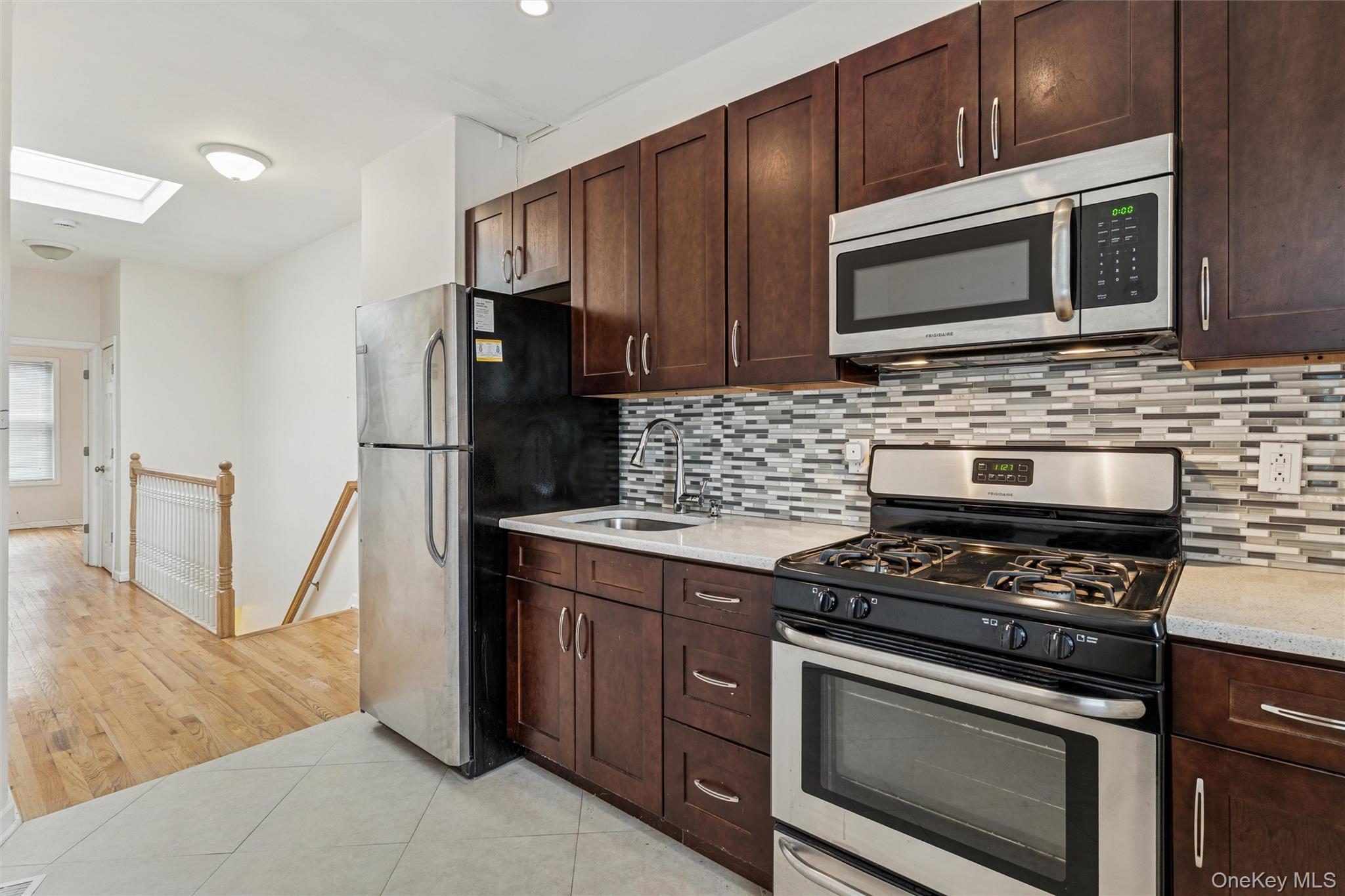 91-25 90th Street Queens, NY 11421 - Photo 21 of 30 Kitchen featuring stainless steel appliances, dark brown cabinets, a skylight, and decorative backsplash
